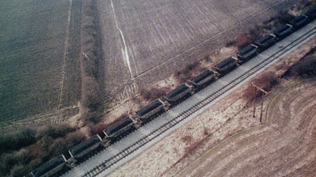 1980年，空中旋转火车载着煤炭在铁轨上移动，穿越广阔的田野/英国视频素材