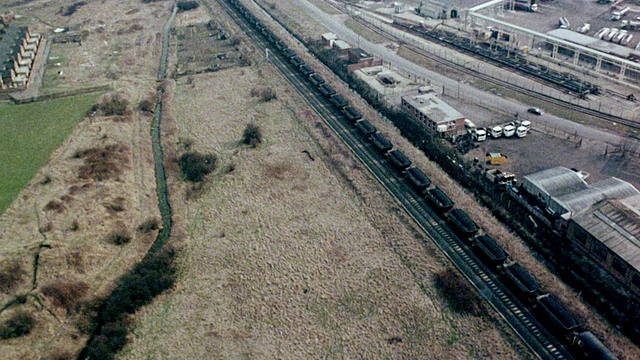 1980年，空中旋转火车载着煤沿着轨道向发电站移动，附近有公路和水道/英国视频素材