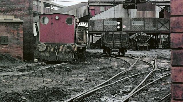 1980年，蒙太奇红色火车载着煤进入煤矿，经过泥泞、车辙的地面，两条链子挂在前景/英国视频素材