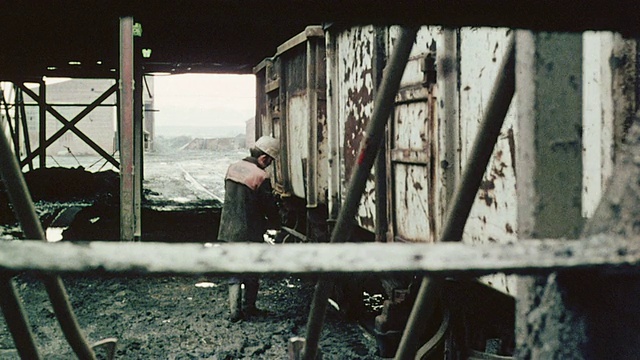 1980年，蒙太奇铁路工人拉着生锈的失控火车上的链条，然后用制动杆推动它，煤炭流入桶/英国视频素材
