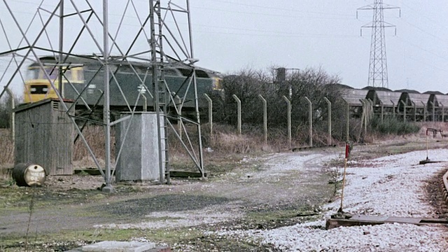 1980年，PAN煤火车沿着铁轨疾驰，经过钢铁塔和空荡荡的火车站场，旁白在讨论火车速度/英国视频素材