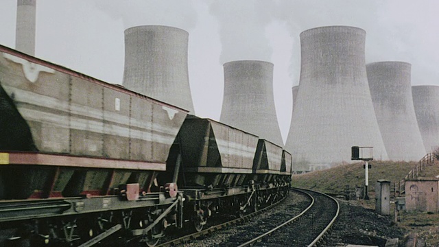 1980年，WS煤炭列车在轨道上行驶，旁边是空轨道，到达有巨大烟囱的发电站，旁白在讨论环线/英国视频素材