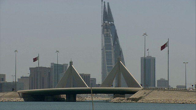 一艘小摩托艇停泊在岸边，旁边是沙伊克·伊萨铜锣桥和巴林世界贸易中心双子塔的天际线视频下载