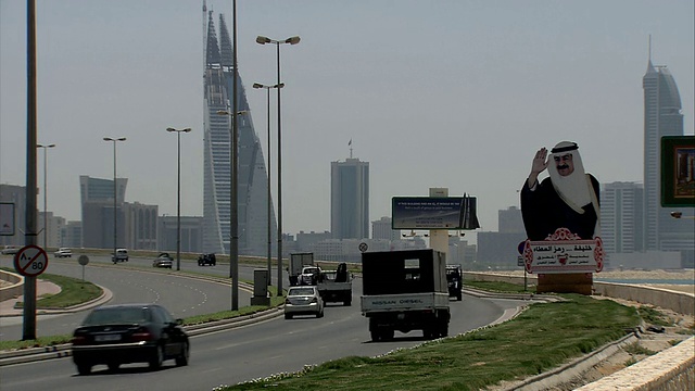繁忙的车辆行驶在高速公路上，路边的大型广告牌上的标志性人物向人们致意，还有巴林世界贸易中心双子塔的天际线视频下载