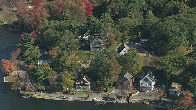 鸟瞰湖岸的滨水住宅，依偎在秋叶环绕的树木之间/美国马萨诸塞州视频下载