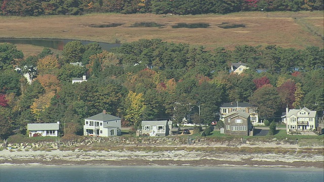 空中村庄坐落在树木与一些秋天的树叶在狭窄的卵石海滩/肯纳邦克港，美国缅因州视频素材