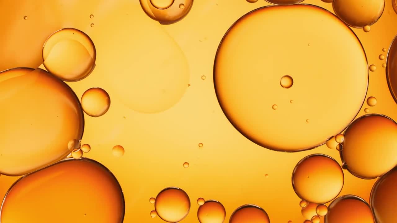 近距离和慢动作的架空视图，将化妆品金黄色的油倒进水池，并在背光背景下用浮动的油滴填充框架视频下载
